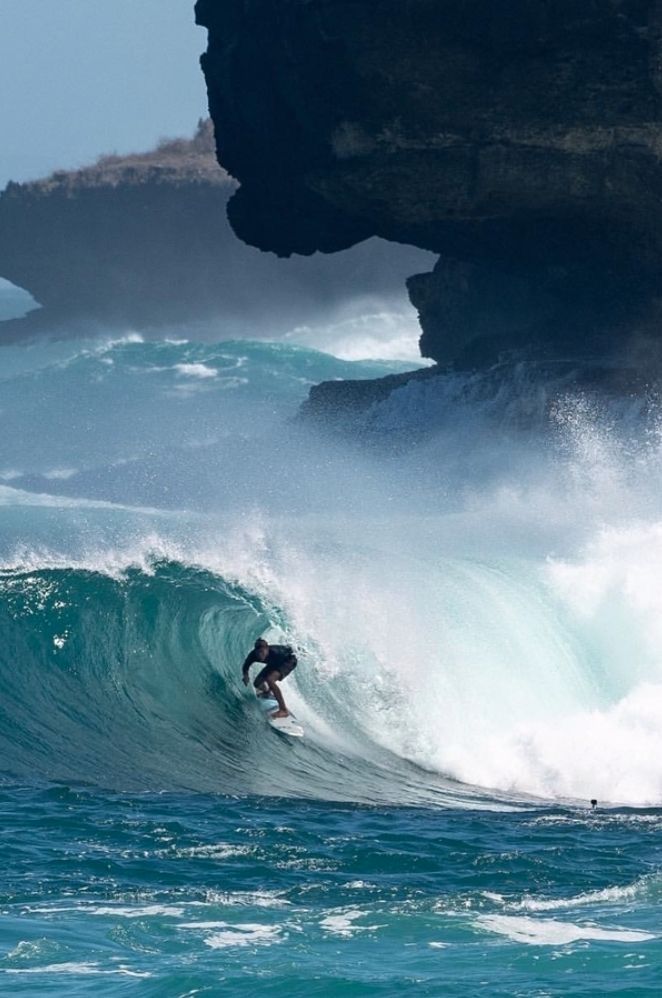 a man riding a wave on top of a surfboard in the ocean next to a cliff