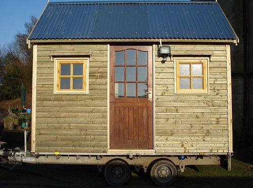 a small wooden house on wheels with a blue roof and two windows in the back