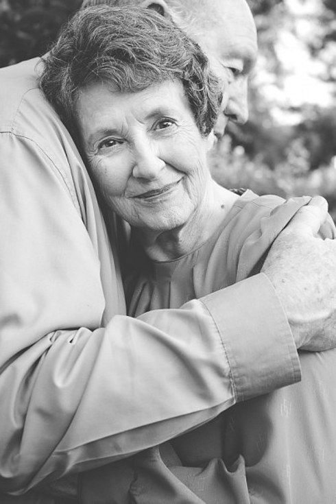 black and white photograph of an older woman hugging her younger man's shoulders in front of trees