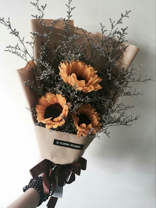 a bouquet of sunflowers is wrapped in brown paper and tied to the wall