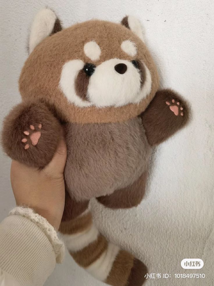 a hand holding a brown and white stuffed animal with paws on it's face