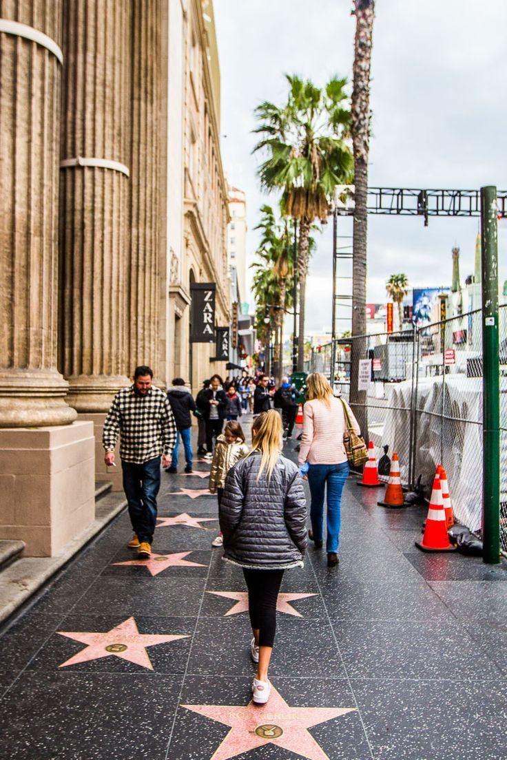 people walking on the hollywood walk of fame with pink stars in front of an old building