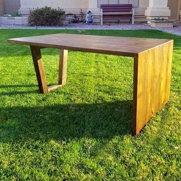 a wooden table sitting on top of a lush green field in front of a house