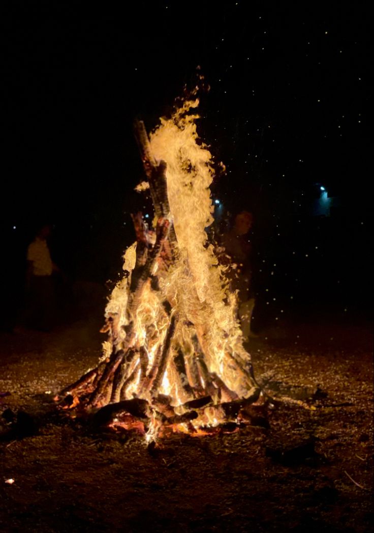 a bonfire is lit in the dark with people around it