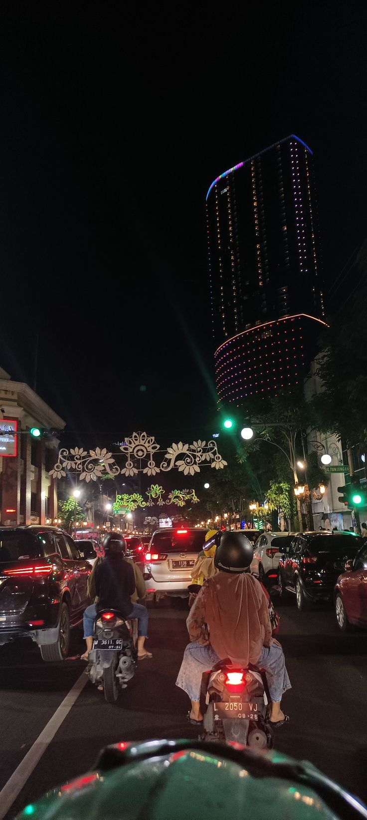 people are riding motorcycles down the street at night with lights on and buildings in the background