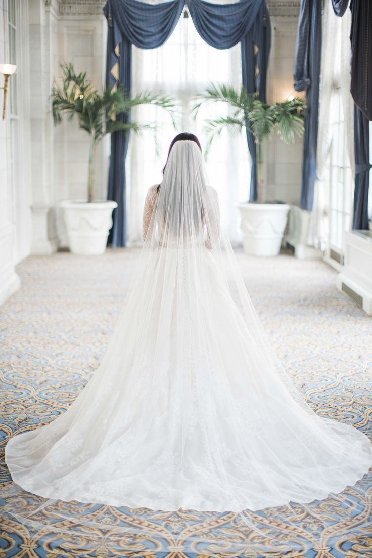 a woman in a wedding dress and veil walking down the aisle with her back to the camera