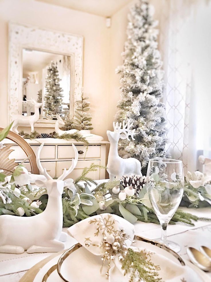 a dining room table decorated for christmas with white and green decorations, deer head plates and silverware