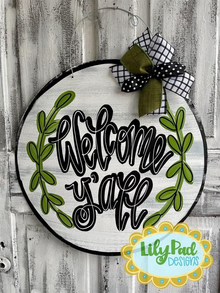 a welcome sign hanging on the side of a wooden door with a green ribbon and bow