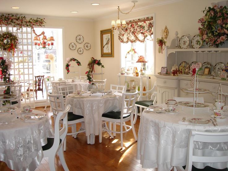 there are many tables and chairs in the room with white tablecloths on them