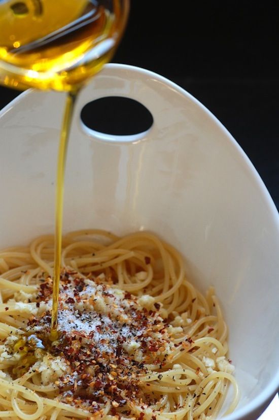 a white bowl filled with pasta and sauce being drizzled over the top