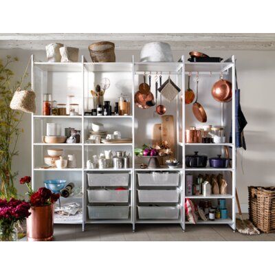 a white shelf filled with pots and pans on top of wooden floor next to plants