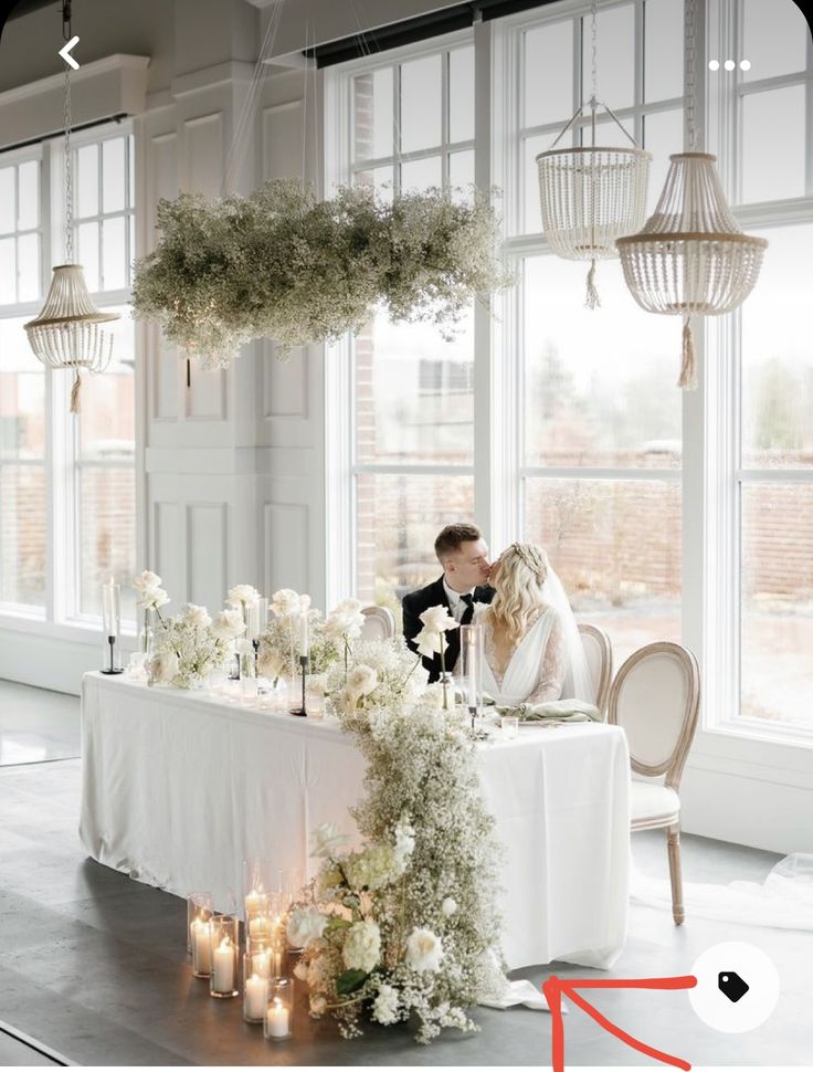 a bride and groom kissing in front of a table with flowers, candles and chandeliers