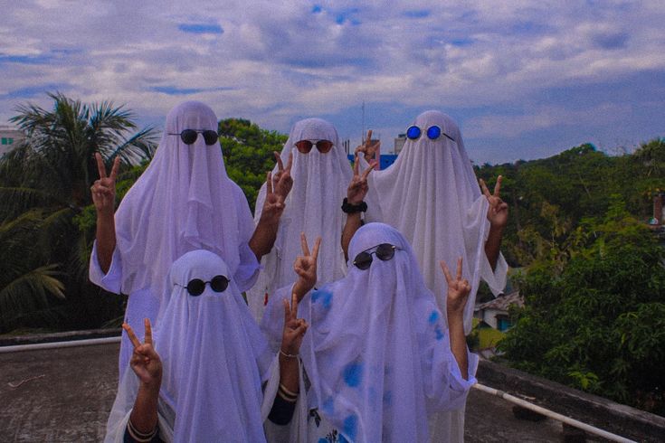 four women in white veils are standing on a roof with their hands raised up