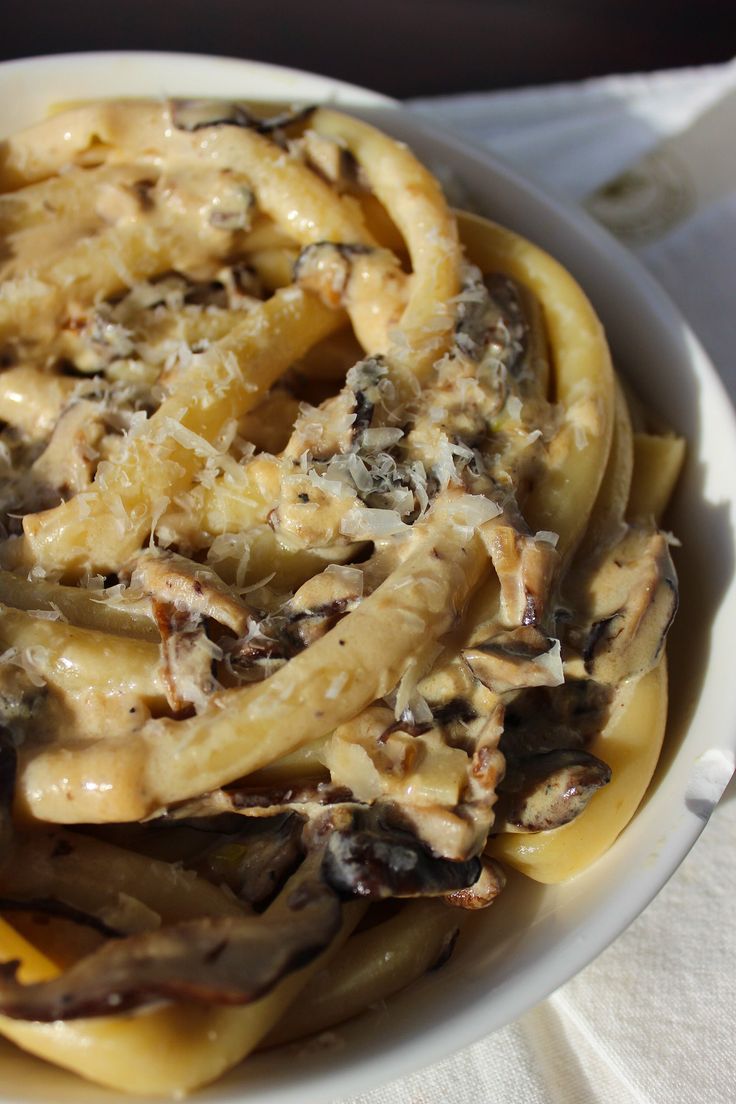 a white bowl filled with pasta covered in cheese and mushrooms on top of a table