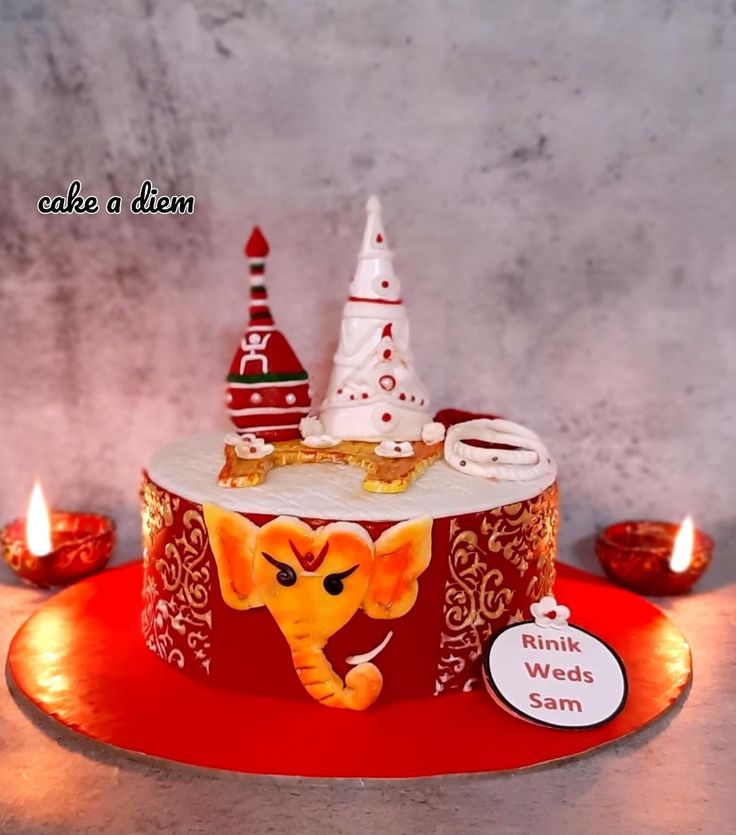 a red and white cake with an elephant on it's side, surrounded by candles