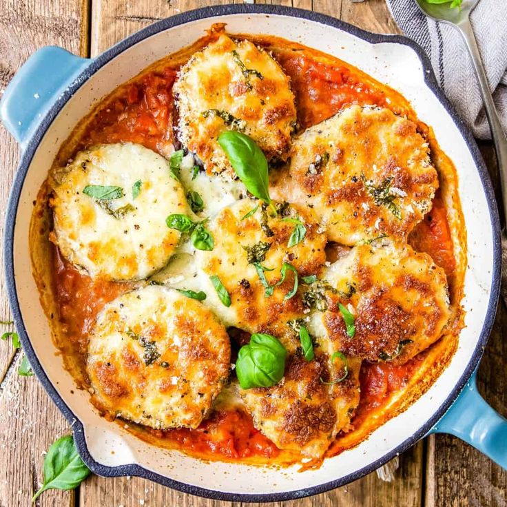 a skillet filled with chicken parmesan and sauce on top of a wooden table