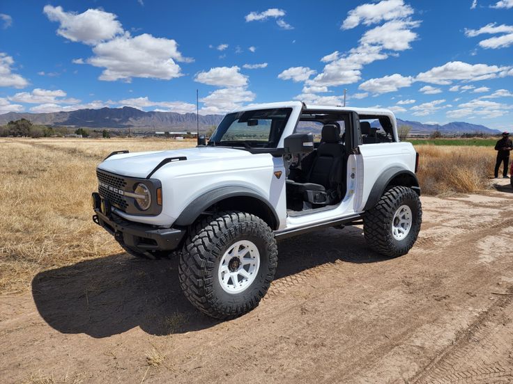 a white truck parked on top of a dirt road next to a dry grass field