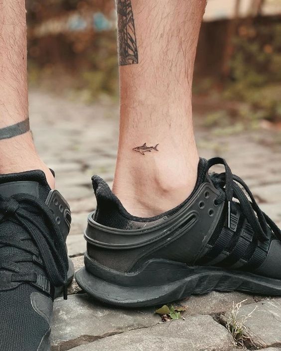 a man's foot with a small tattoo on his left leg and black sneakers