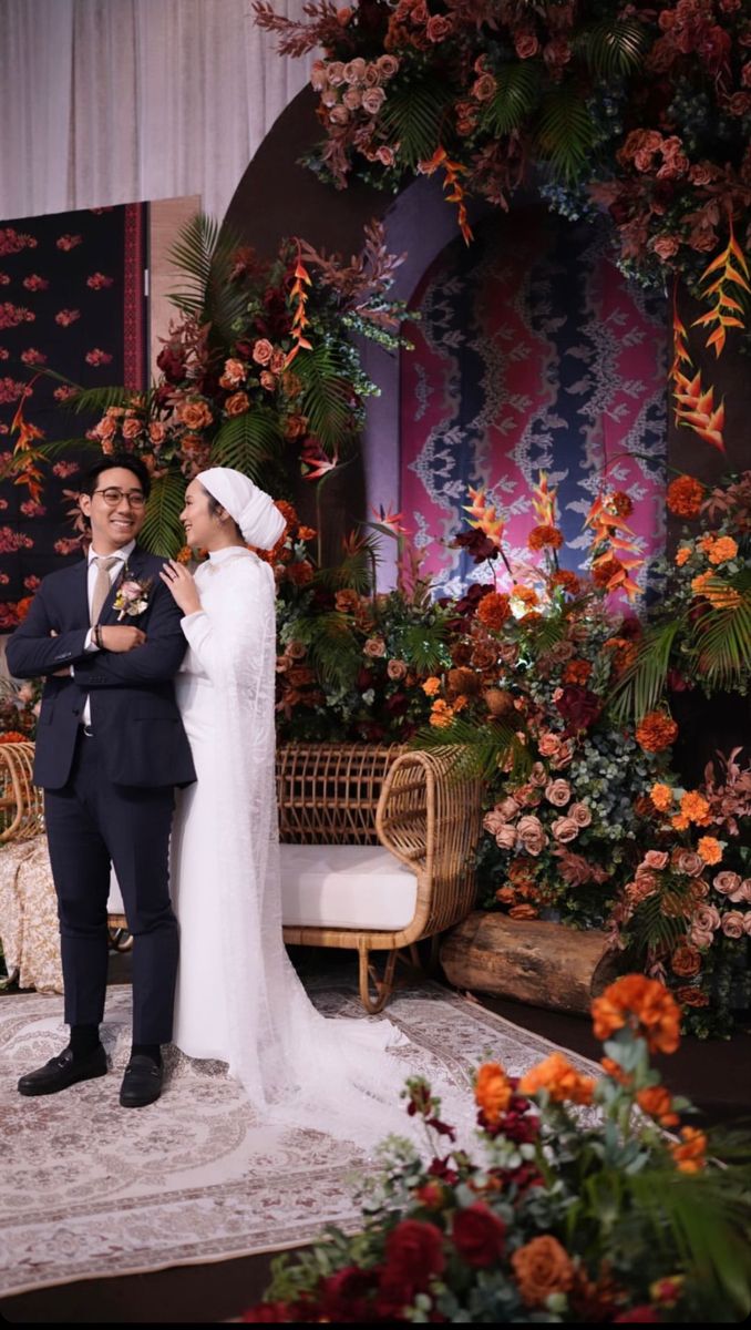 two people standing next to each other in front of flowers and plants on a stage