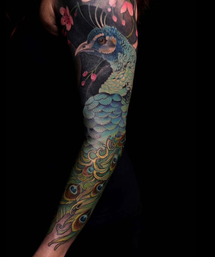 a woman's arm covered in tattoos with a peacock and flowers on the side