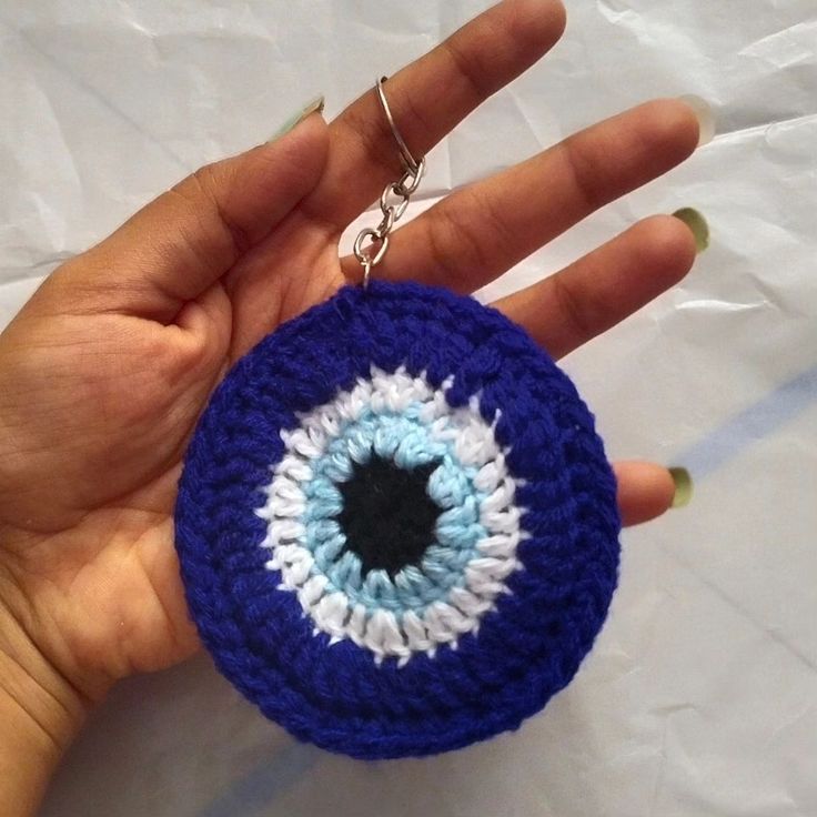 a hand holding a crocheted keychain with an evil eye on it