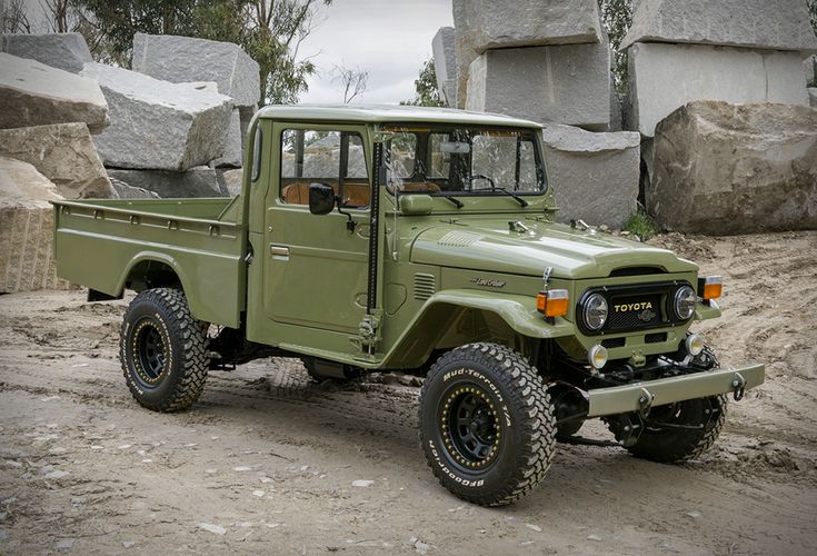 an army green truck parked on top of a dirt field next to rocks and trees