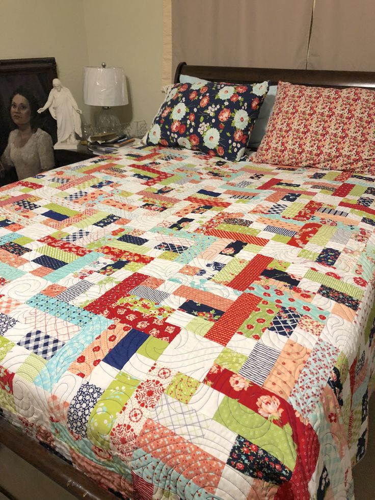 a bed with a colorful quilt on top of it and a woman sitting in the background