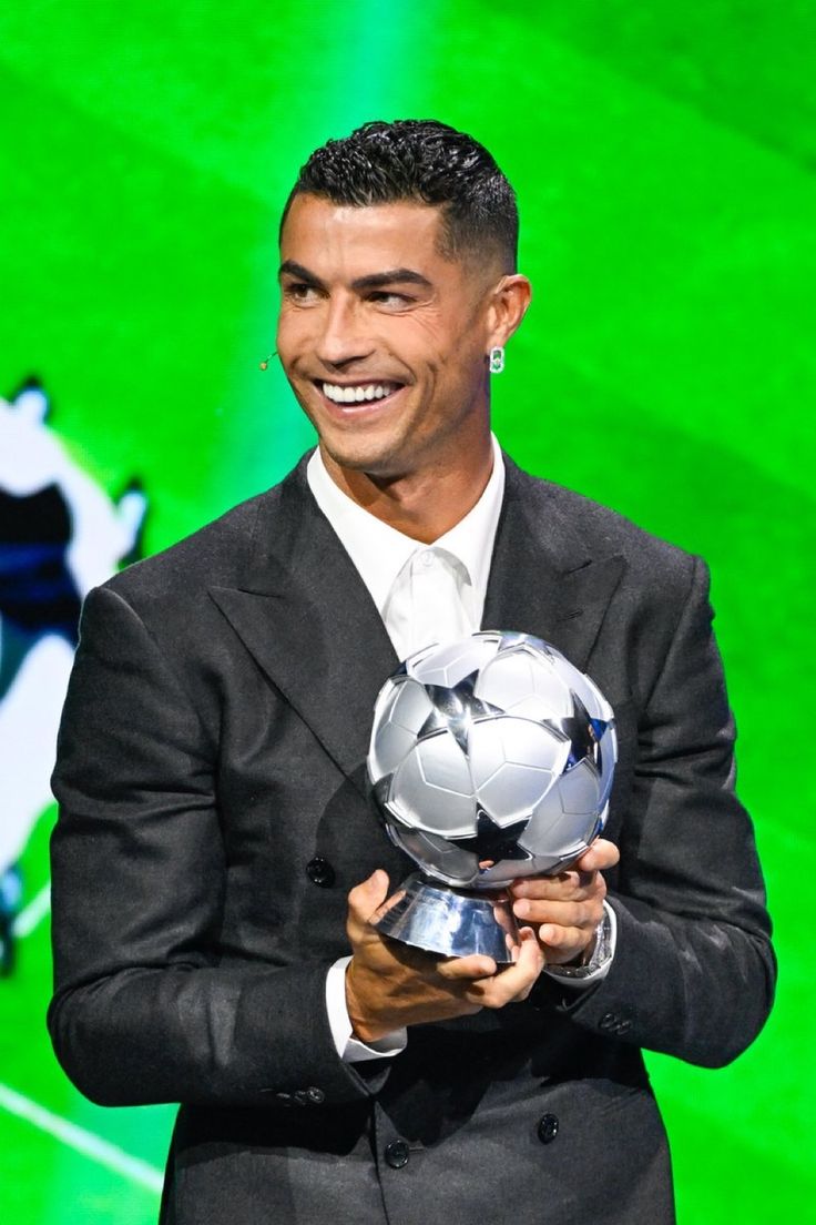 a man in a suit holding a soccer ball and smiling at the camera while standing on a stage