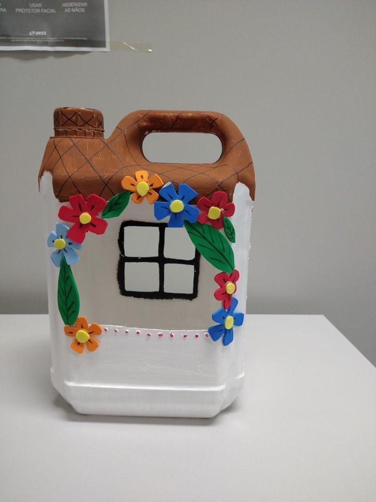 a plastic container decorated with flowers and a house on it's side, sitting on a table