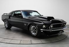 a black muscle car sitting on top of a cement floor next to a white wall