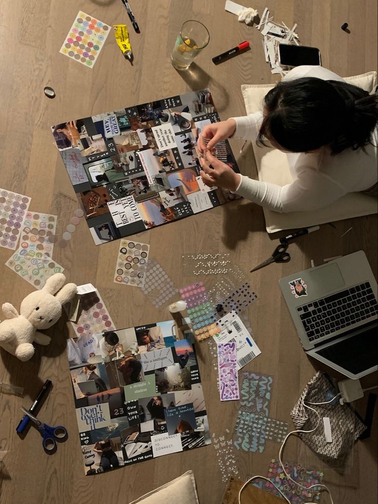 a woman sitting at a desk covered in pictures and other things on the floor next to a laptop computer