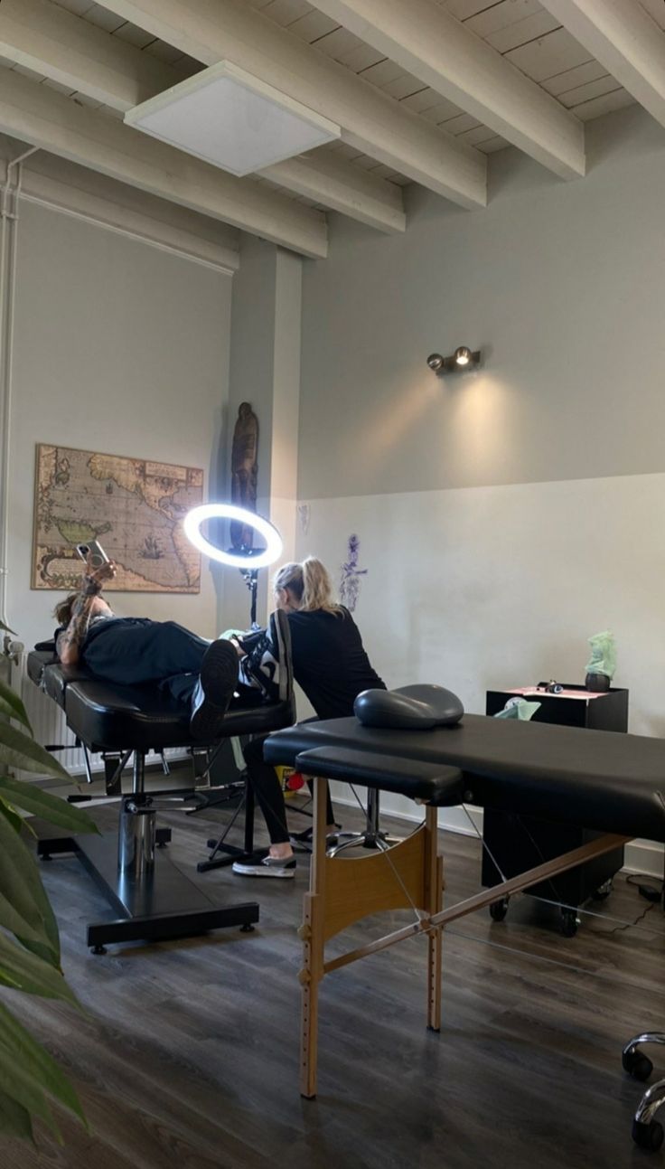 a woman sitting in a chair with a magnifying light on her head while another person sits at a desk