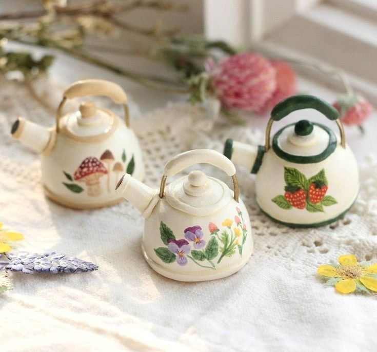 three tea kettles sitting on top of a white doily next to flowers and leaves