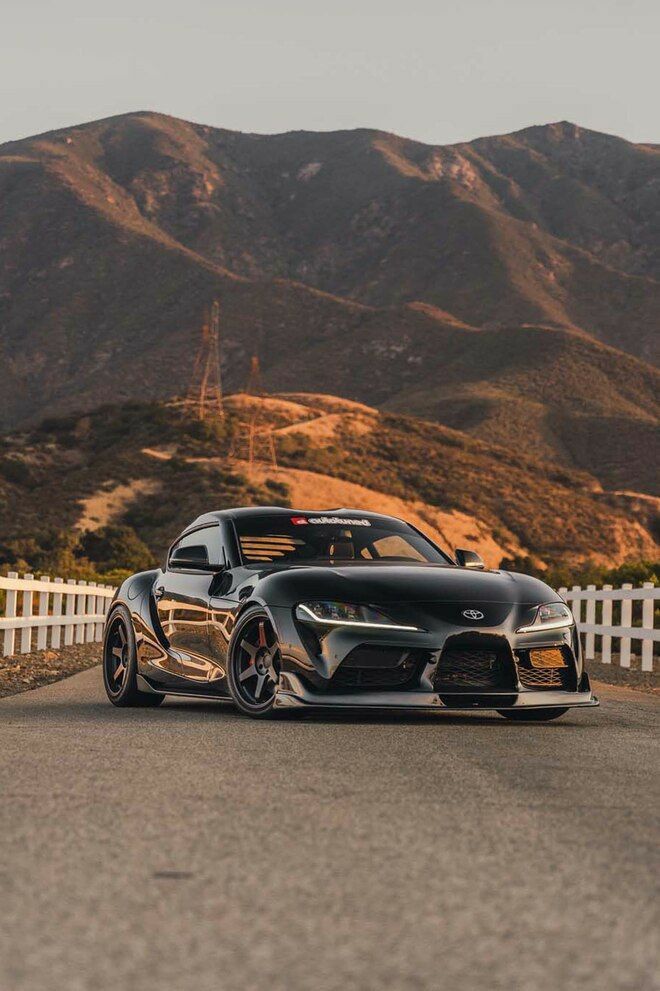 a black sports car parked in front of a white picket fence with mountains in the background