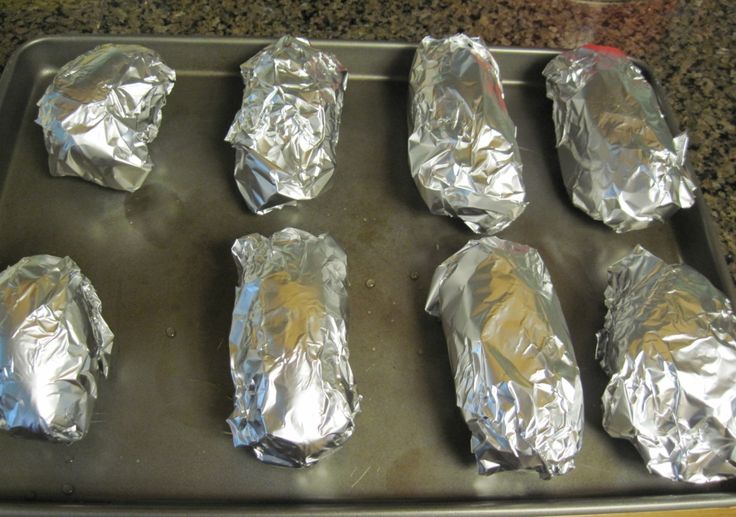 six aluminum foil wrapped hot dogs on a baking sheet, ready to go in the oven