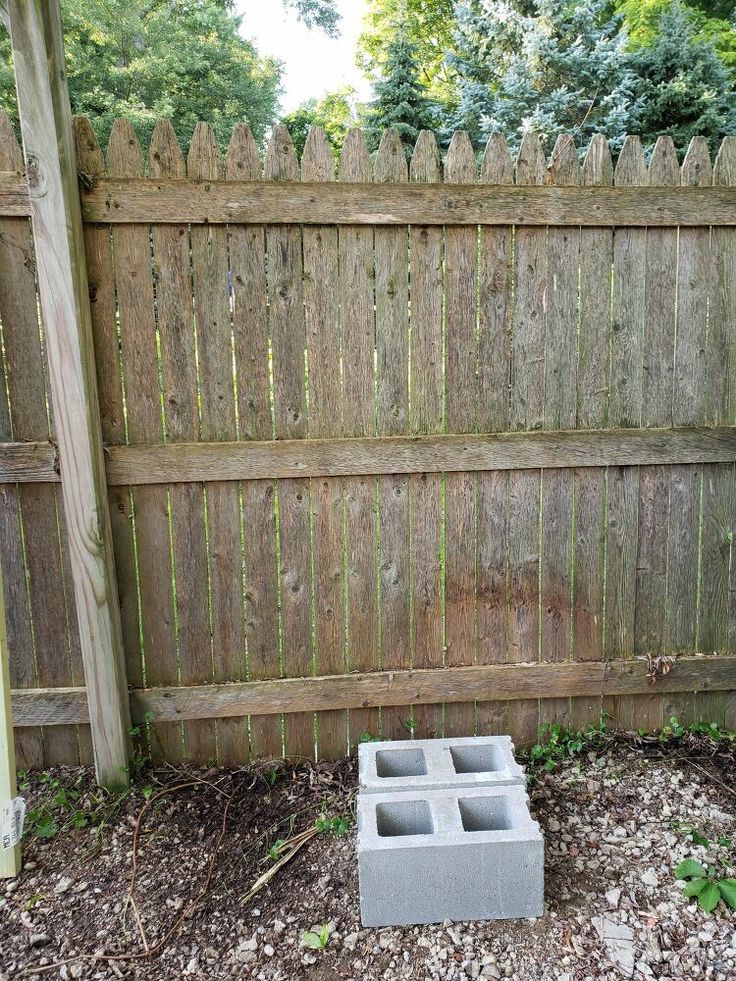 an empty cinder block sitting in the middle of a yard next to a wooden fence