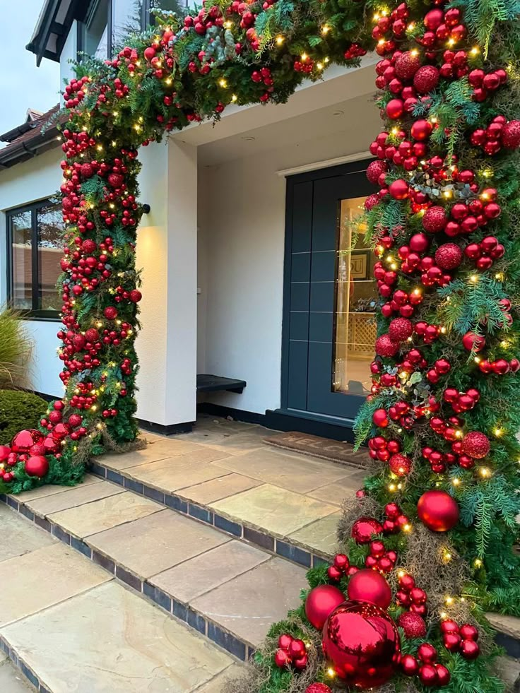 a house decorated for christmas with red ornaments and greenery on the front door steps