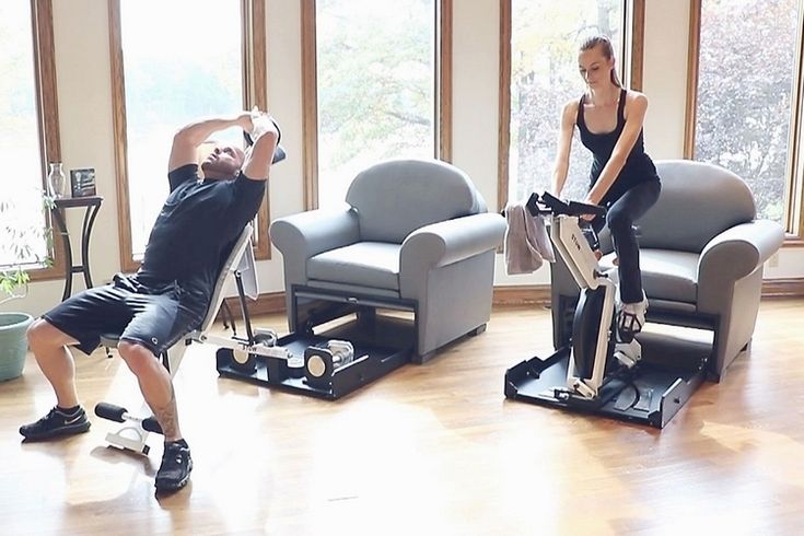 a man and woman are exercising on exercise bikes in the living room with large windows