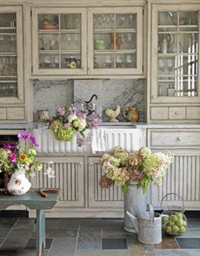 a kitchen with white cabinets and flowers in vases on the counter top next to a green table