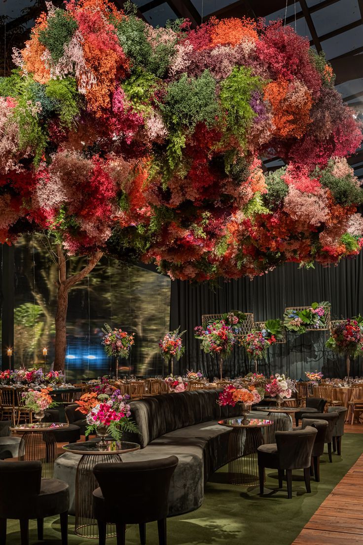 a room filled with lots of tables and chairs covered in colorful flowers hanging from the ceiling