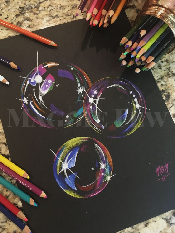 some colored pencils are laying on top of a black paper with an image of bubbles