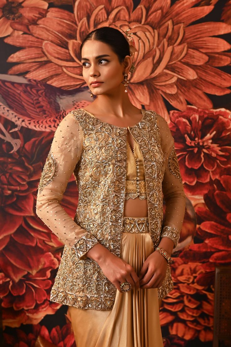 This Gold Co-ord set is the way to hop on the bold and versatile trend, that modern women prefer. Paired with a waistcoat style top along with a heavily embroidered jacket detailed with silver and golden hue and for the bottom a dhoti-style draped skirt giving you that chic regal look. Gold foil printed sleeveless blouse with embroidered border and handmade buttons on the centre front Front Open jacket with gold foil print heavily embellished with dabka & nakshi Waistcoat style bustier Dhoti-sty Reception Palazzo Set With Gold Embroidery, Designer Raw Silk Palazzo Set With Gold Embroidery, Traditional Designer Palazzo Set With Gold Embroidery, Designer Palazzo Set With Gold Embroidery For Eid, Reception Choli With Zari Work And Front Open, Front Open Choli With Zari Work For Reception, Festive Designer Palazzo Set With Gold Embroidery, Traditional Palazzo Set With Gold Embroidery For Designer Wear, Elegant Gold Embroidered Palazzo Set With Traditional Drape