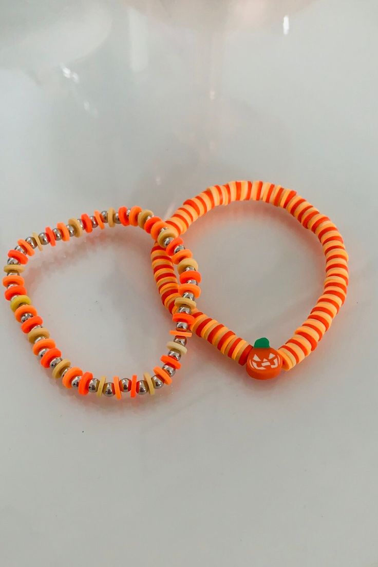 two orange and yellow bracelets sitting on top of a white table next to each other