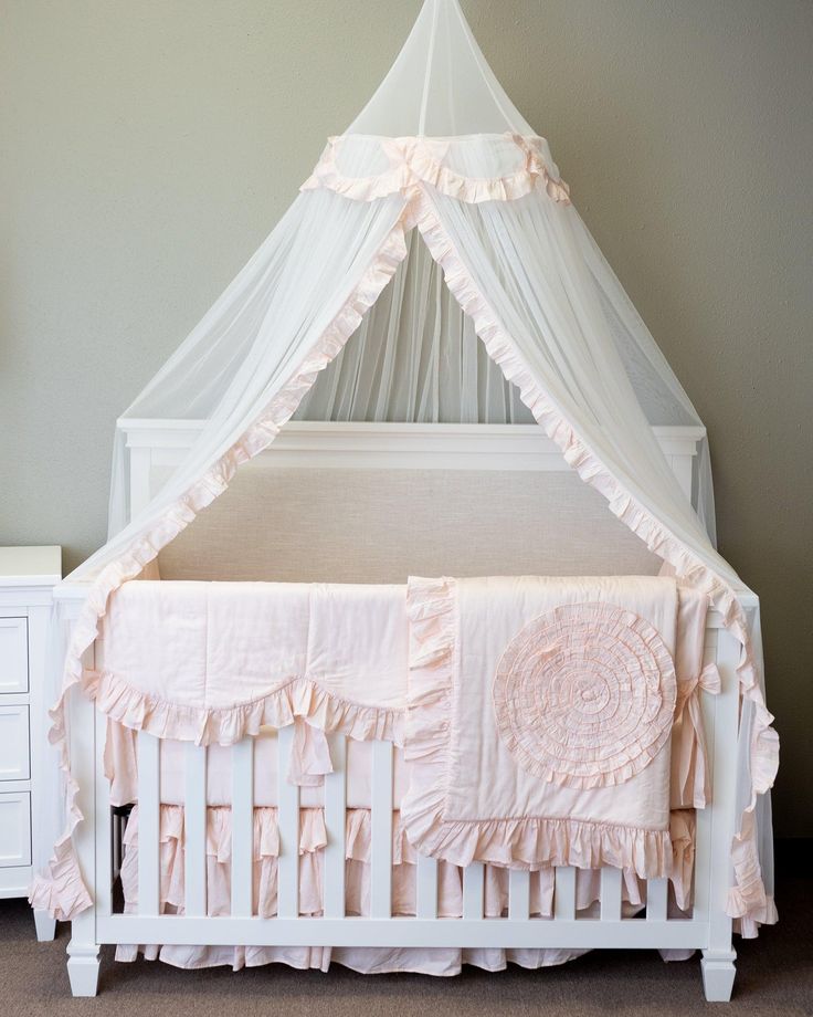 a white crib with pink ruffled bedding and a canopy over the crib