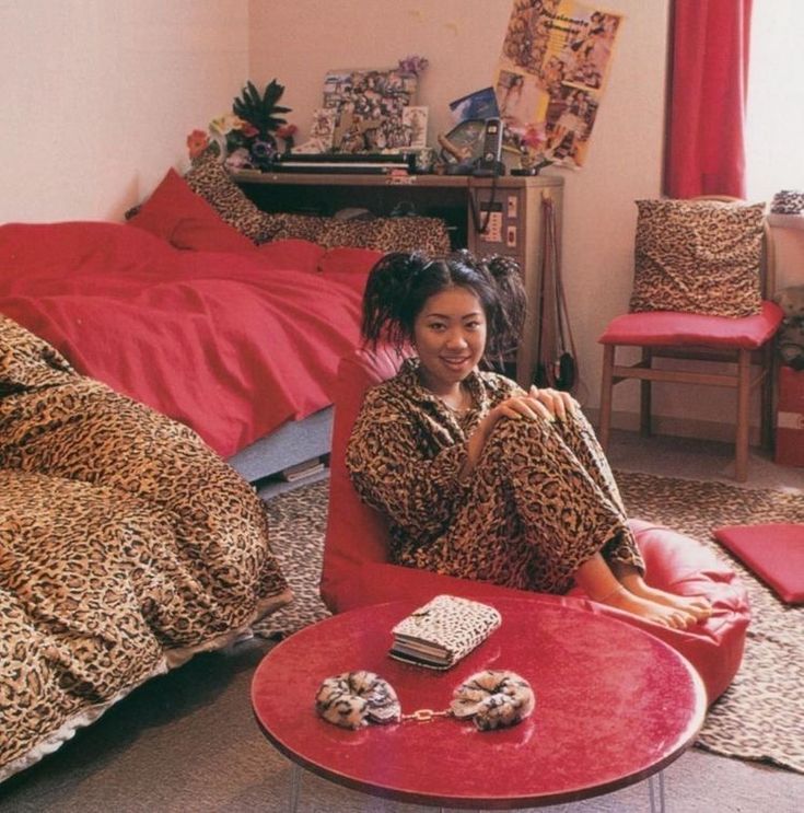 a woman sitting on the floor in front of a red table and leopard print bedding