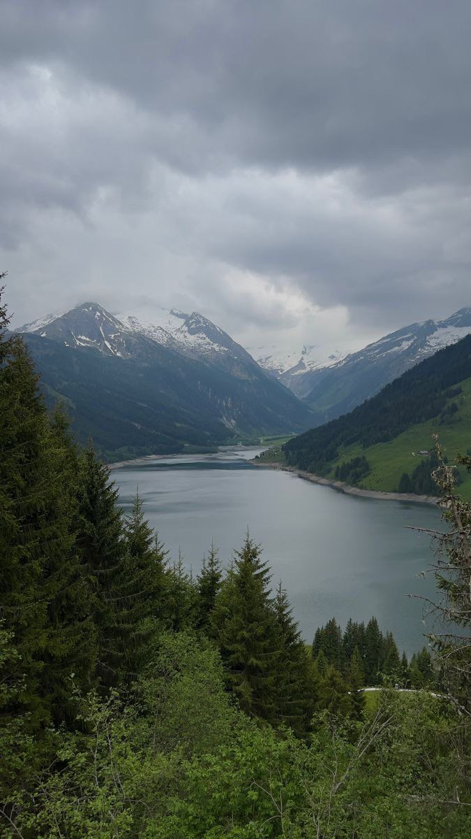 a lake surrounded by trees and mountains under a cloudy sky