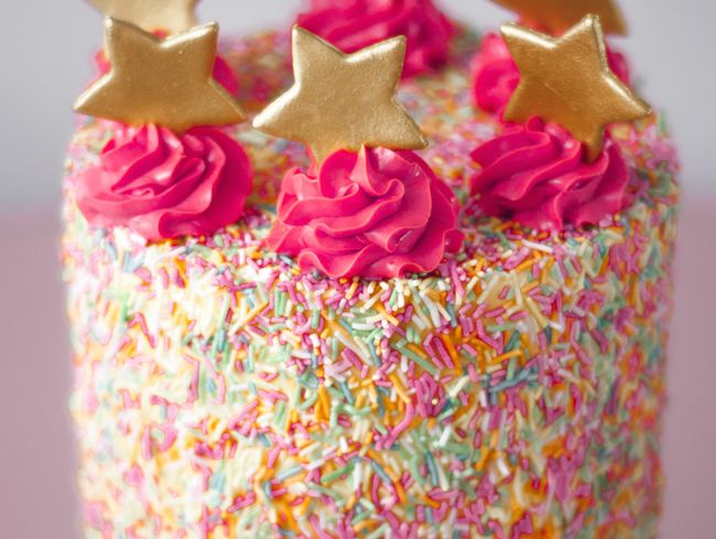 a birthday cake with sprinkles and gold stars on top is decorated with pink frosting