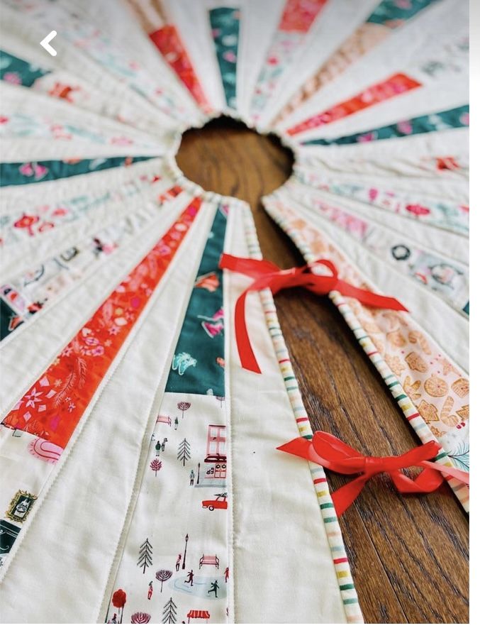 a close up of a quilted fan on a wooden table with red ribbon around it