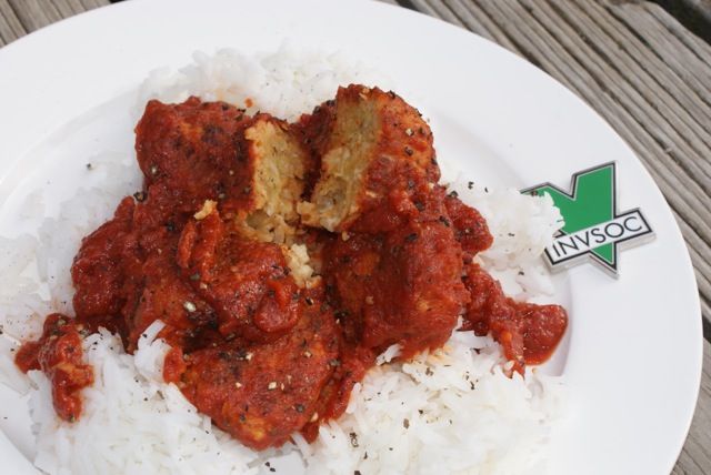 a white plate topped with rice and meat covered in marinara sauce on top of a wooden table