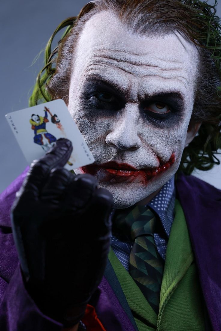 a man dressed as the joker holding up a card